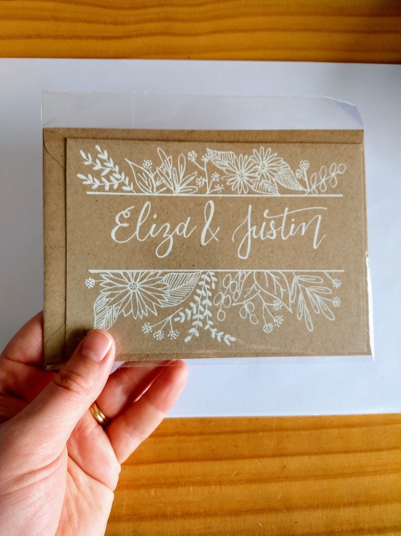 May include: A brown card with white floral designs and the text "Eliza & Justin" written in white calligraphy.