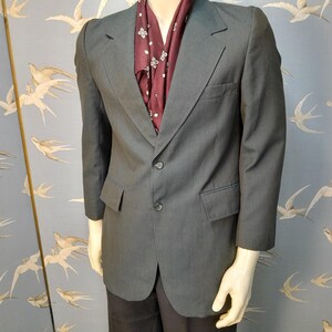 May include: A dark grey blazer with a two-button fastening, notched lapels, and front pockets. A burgundy scarf with a white floral pattern is worn underneath. The blazer is displayed on a mannequin.