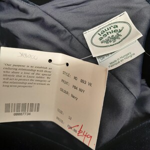 May include: A navy blue velvet dress with a Laura Ashley tag. The tag has the text "Laura Ashley" in a white font with a green leaf design. The tag also has the text "Made in Hungary" and "Fabriqu&eacute; en Hongrie". The dress has a price tag attached with the text "STYLE: MD 093 VK", "PRINT: P04 NVY", "COLOUR: Navy", "SIZE: 12", "PRICE: &pound;98.00", and "&pound;49".