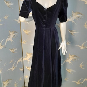 May include: A navy blue velvet dress with a sweetheart neckline and short puffed sleeves. The dress has a fitted bodice and a flowing skirt.