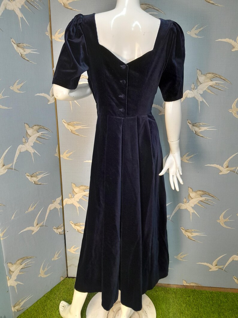 May include: A navy blue velvet dress with a sweetheart neckline and short puffed sleeves. The dress has a fitted bodice and a flowing skirt.