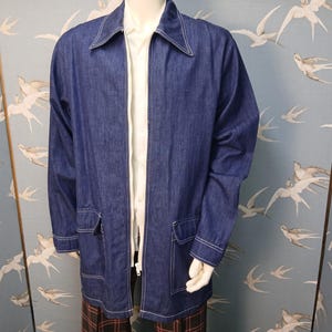 May include: A dark blue denim jacket featuring a pointed collar, a full-length front zipper, and two large patch pockets with flaps on the lower front. The jacket is accented with white contrast stitching along the seams, pockets, and cuffs.