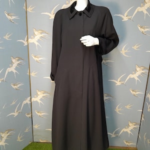 May include: A long black coat with a velvet collar and cuffs. The coat has a single button closure and a straight silhouette.