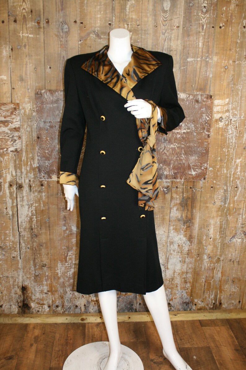 K&ouml;nnte beinhalten: Ein schwarzes, zweireihiges Kleid mit einem Tigermuster-Kragen und einer passenden Sch&auml;rpe. Das Kleid hat goldene Kn&ouml;pfe und einen knielangen Rock.