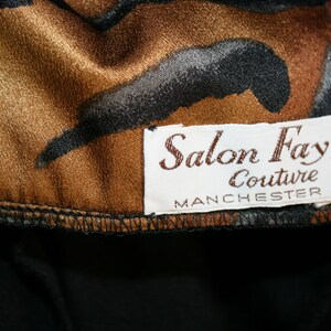 K&ouml;nnte beinhalten: Ein brauner und schwarzer gemusterter Stoff mit einem wei&szlig;en Etikett, auf dem "Salon Fay Couture Manchester" steht.