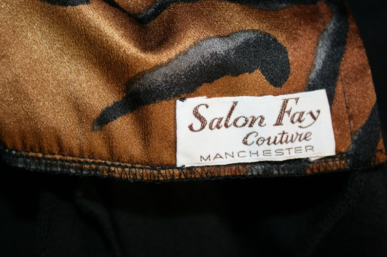 K&ouml;nnte beinhalten: Ein brauner und schwarzer gemusterter Stoff mit einem wei&szlig;en Etikett, auf dem "Salon Fay Couture Manchester" steht.