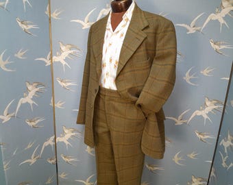 May include: A brown and green checked suit jacket and matching trousers. The jacket has a single button fastening and a pocket on the left side. The trousers have a straight leg.