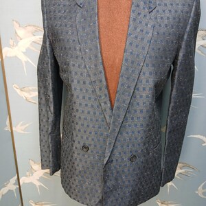 May include: A blue blazer with a subtle checkered pattern. The double-breasted jacket has two rows of buttons and notched lapels. The fabric has a slight sheen, and the blazer is displayed on a mannequin.