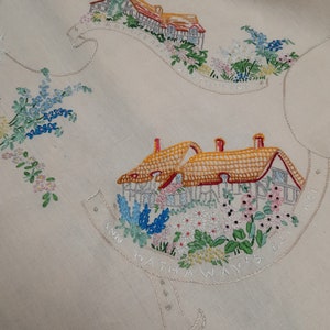 May include: White linen tablecloth with embroidered images of houses and flowers. The text "Ann Hathaway's Way is the Best Way" is embroidered around the bottom of the houses.