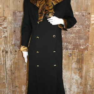 K&ouml;nnte beinhalten: Ein schwarzes, zweireihiges Kleid mit einem goldenen Schal-Kragen mit Tigermuster und goldenen Kn&ouml;pfen. Das Kleid hat lange &Auml;rmel mit goldenen Manschetten mit Tigermuster.