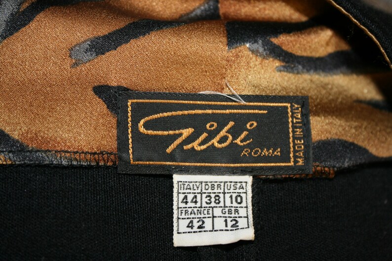 K&ouml;nnte beinhalten: Ein schwarzes Etikett mit dem Text "Tibi Roma" und "Made in Italy". Ein kleineres wei&szlig;es Etikett mit Gr&ouml;&szlig;enumrechnungen in italienischer, franz&ouml;sischer, britischer und amerikanischer Gr&ouml;&szlig;e.