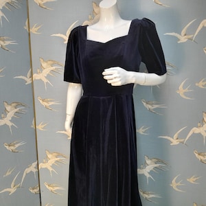 May include: A navy blue velvet dress with a square neckline and short puff sleeves. The dress has a fitted bodice and a full skirt.