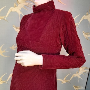 May include: A maroon velvet dress with a high neck and long sleeves. The dress has a textured, quilted pattern.