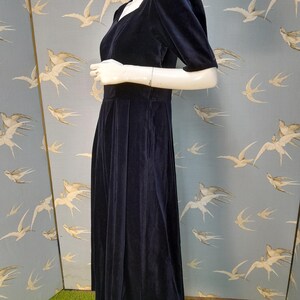 May include: A navy blue velvet dress with a square neckline and short puff sleeves. The dress has a fitted bodice and a flowing skirt.