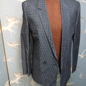 May include: A double-breasted blazer in a blue and silver checked pattern. The jacket is displayed on a mannequin, highlighting its tailored fit and classic design. The blazer features two rows of buttons and a notched lapel.