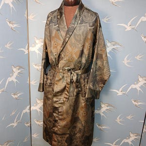 May include: A long, patterned robe in shades of brown, grey, and gold, with a matching belt and pockets. The robe is displayed on a mannequin against a light blue background with a bird pattern.