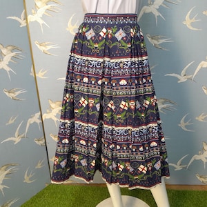 May include: A navy blue, pleated skirt with a repeating pattern of flags, crests, and floral elements. The skirt has a white hem and is displayed on a mannequin. The background features a light blue wall with a bird pattern.