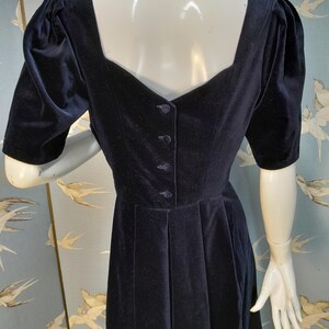 May include: A black velvet dress with a square neckline and puffed sleeves. The dress has a button closure down the back and a fitted bodice.