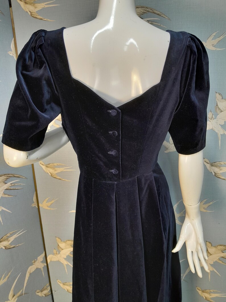 May include: A black velvet dress with a square neckline and puffed sleeves. The dress has a button closure down the back and a fitted bodice.