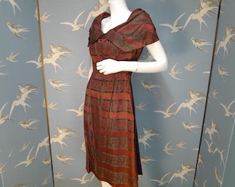 May include: A vintage maroon dress with a patterned design and a unique collar. The dress features horizontal stripes in shades of maroon and dark green. The dress is displayed on a mannequin.