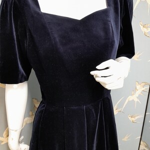 May include: A black velvet dress with a square neckline and short puff sleeves. The dress has a fitted bodice and a full skirt.