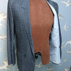 May include: A blue and navy checked double-breasted blazer. The jacket is displayed on a brown mannequin, revealing a light blue lining. The blazer has a classic notched lapel and two front buttons. The jacket's measurements are in centimeters.
