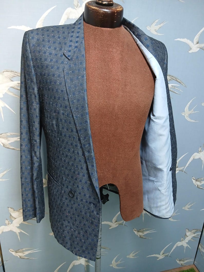 May include: A blue and navy checked double-breasted blazer. The jacket is displayed on a brown mannequin, revealing a light blue lining. The blazer has a classic notched lapel and two front buttons. The jacket's measurements are in centimeters.