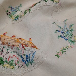 May include: A white linen tablecloth with embroidered floral designs and a group of birds in orange and yellow.