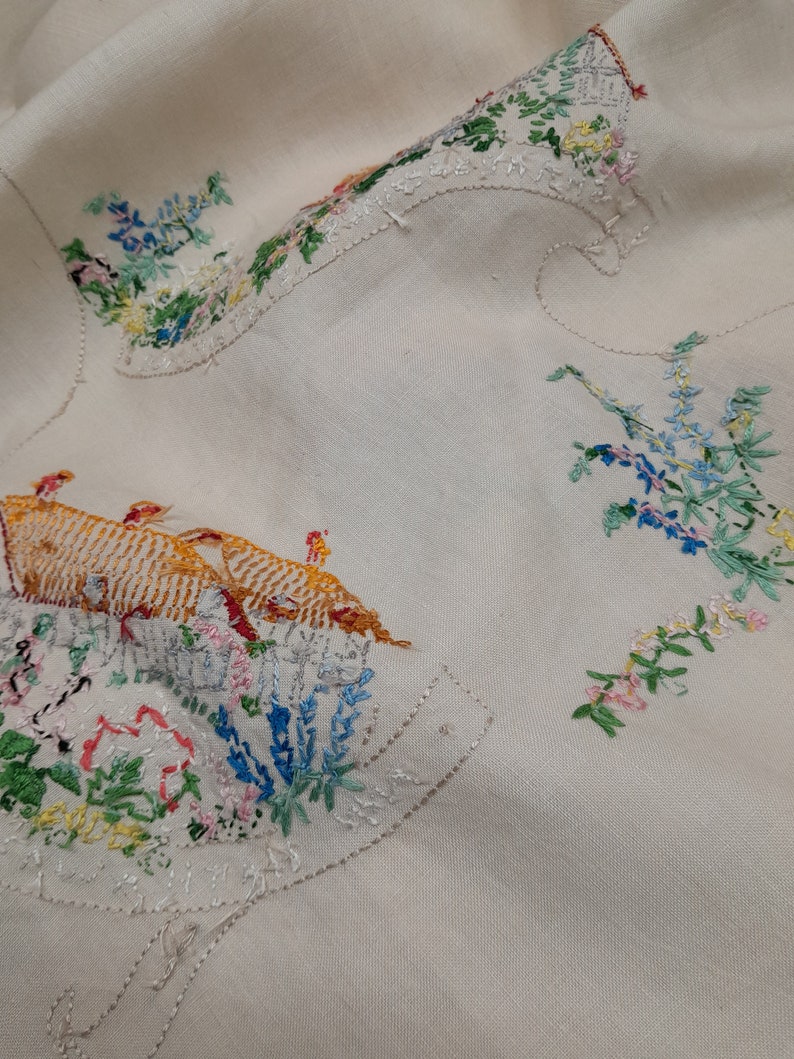 May include: A white linen tablecloth with embroidered floral designs and a group of birds in orange and yellow.