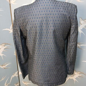 May include: A dark blue blazer with a textured, square pattern. The back of the jacket is visible, showcasing the tailored fit and the subtle sheen of the fabric. The blazer is displayed on a mannequin.
