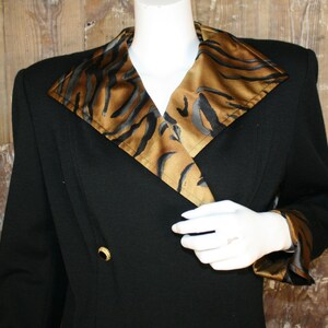K&ouml;nnte beinhalten: Ein schwarzer Blazer mit einem gro&szlig;en, breiten Kragen, der mit einem braunen und schwarzen Tiermusterstoff gef&uuml;ttert ist. Der Blazer hat einen zweireihigen Verschluss mit einem goldenen Knopf.