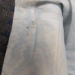 May include: A close-up view of a garment's interior and exterior. The lining is a pale blue fabric with a marbled design. The outer fabric is dark with blue and red flecks. Some staining is visible on the lining.