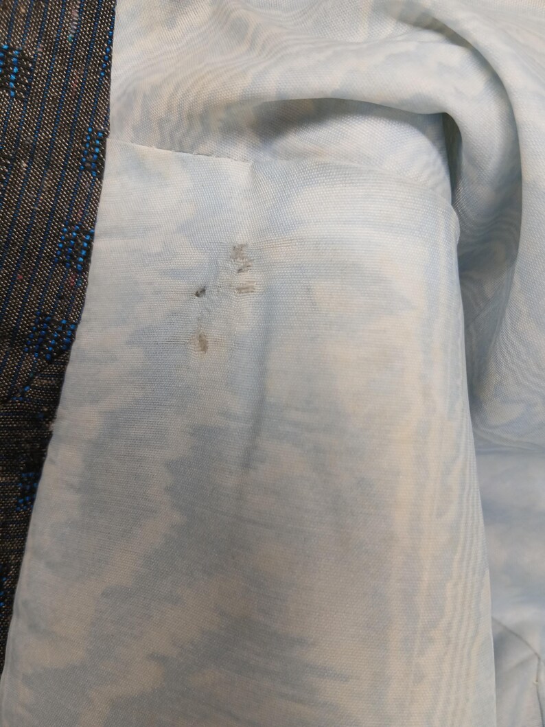 May include: A close-up view of a garment's interior and exterior. The lining is a pale blue fabric with a marbled design. The outer fabric is dark with blue and red flecks. Some staining is visible on the lining.