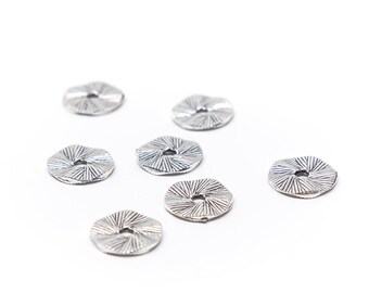 May include: Eight silver-toned metal beads with a decorative, sunburst-like design. The beads are scattered on a white background.
