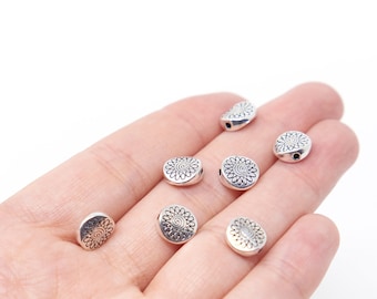 May include: Silver metal round beads with a decorative floral design. The beads have a hole in the center for stringing.