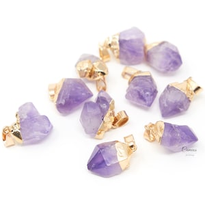May include: A group of ten amethyst crystal pendants with gold-toned metal accents. The crystals are various shades of purple and have a rough, natural texture.
