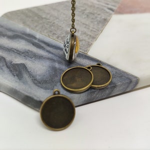 Peut inclure: Quatre pendentifs ronds en métal de couleur bronze avec une boucle en haut. Les pendentifs sont sur une surface en marbre.