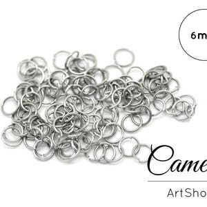 Puede incluir: Un montón de anillos de salto plateados de 6 mm. La imagen incluye el texto "Cameos ArtShop". Estos pequeños anillos circulares se utilizan para la fabricación de joyas y manualidades.
