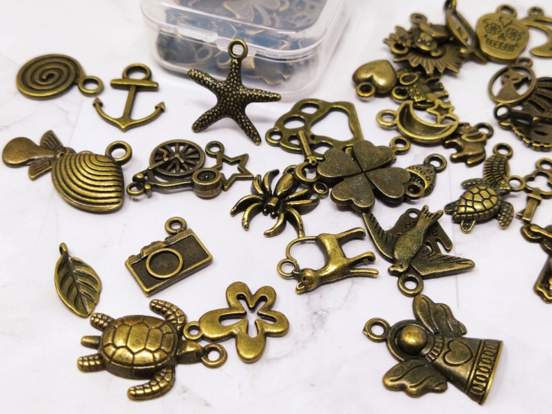 May include: Assortment of bronze-colored metal charms with various designs, including a camera, a turtle, a flower, a bird, a deer, a spider, a clover, a crescent moon, a star, a shell, a wheel, a leaf, an anchor, a spiral, and an angel.