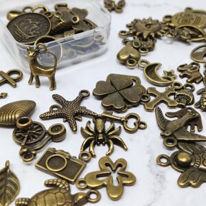 May include: A collection of antique bronze charms and pendants, including a cat, a four-leaf clover, a bird, a cross, a crescent moon, a starfish, a bicycle, a flower, and a seahorse.
