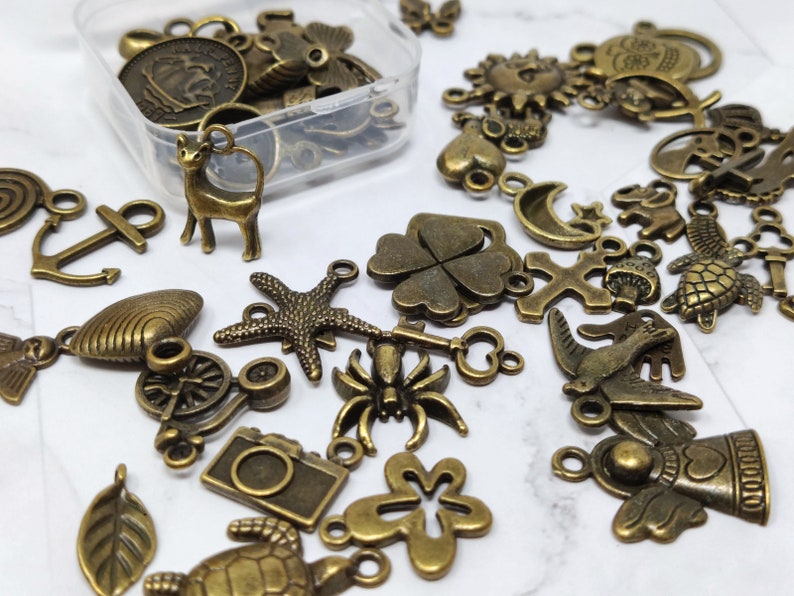 May include: A collection of antique bronze charms and pendants, including a cat, a four-leaf clover, a bird, a cross, a crescent moon, a starfish, a bicycle, a flower, and a seahorse.