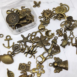 May include: A collection of antique gold-toned metal charms, including a star, a clover, a sun, a heart, a turtle, a fish, a spider, a camera, a leaf, a spiral, an anchor, a wheel, a bird, a crown, a skull, a bell, a hand-made tag, and a religious cross.