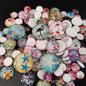 Puede incluir: Surtido de cabujones de vidrio coloridos con varios dise&ntilde;os, incluyendo patrones florales, formas geom&eacute;tricas y un flamenco con el texto "Keep Going".