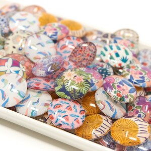 Puede incluir: Una colecci&oacute;n de cabujones de vidrio redondos y coloridos con varios patrones, incluyendo dise&ntilde;os florales, geom&eacute;tricos y abstractos. Los cabujones est&aacute;n dispuestos en un plato de cer&aacute;mica blanca.