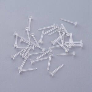 May include: A pile of clear plastic earring posts. The posts are about 1 inch long and have a small, flat head.