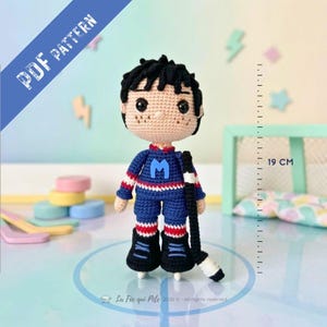 Peut inclure: Une poupée au crochet représentant un joueur de hockey aux cheveux noirs, portant un maillot bleu avec un M bleu clair, un short bleu et des patins noirs. La poupée tient une crosse de hockey noire et mesure 19 cm. Texte PDF PATTERN inclus.