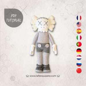 Peut inclure: Une poupée au crochet faite à la main, inspirée de KAWS. La poupée a une tête blanche avec des yeux barrés, un corps gris, un short gris et des gants et chaussures blancs. Le texte "PDF TUTORIAL" est visible. Le site web www.lafeequipete.com est en bas.