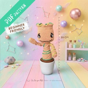 May include: A crochet amigurumi figure of a tree-like character with large black eyes, tan yarn body, and green accents, standing in a white ribbed pot. A ruler graphic indicates a height of 20 cm. Text reads PDF PATTERN BEGINNER FRIENDLY.