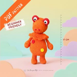 Peut inclure: Une poupée en crochet orange avec un col à volants, des taches oculaires rouges et des points circulaires jaunes et rouges. La poupée mesure 17 cm de haut, comme indiqué par une règle. Le texte indique PDF PATTERN et BEGINNER FRIENDLY.