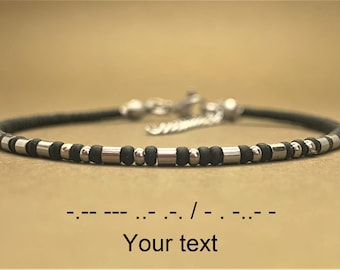 May include: A black and silver beaded bracelet with a silver clasp. The bracelet is made with small black beads and silver beads that are slightly larger. The bracelet has a silver chain attached to the clasp. The text "Your text" is written below the bracelet, along with a line of Morse code.